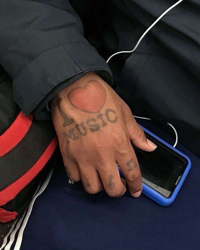 Hand with music-themed tattoos holding a phone on New York subway, showcasing the unique things people carry.