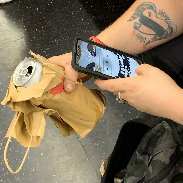 Person on New York subway holding a phone and a crumpled paper bag with a soda can inside.
