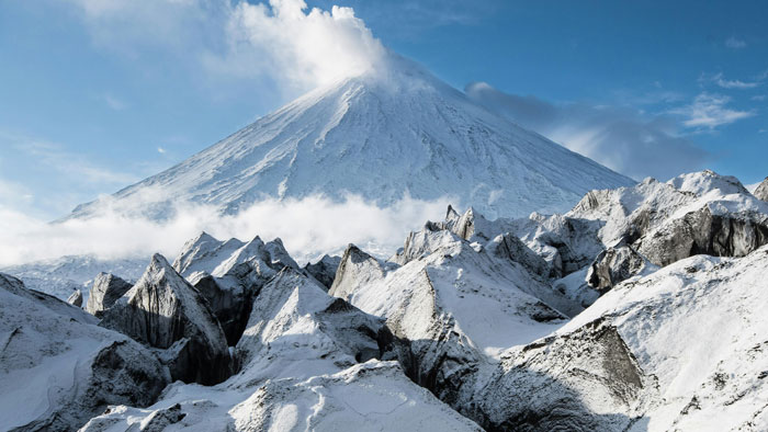Snow-covered volcano under a blue sky with clouds, illustrating the mystery of the time when the sun turned blue. Snow-covered volcano under a blue sky with clouds, illustrating the mystery of the time when the sun turned blue.