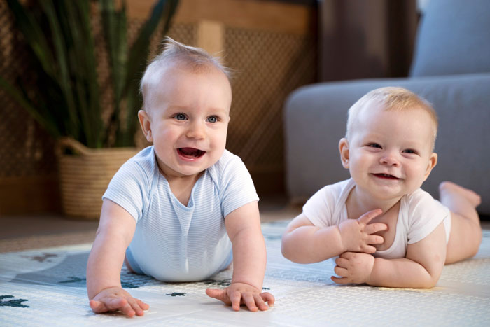 Two smiling babies lying on a carpet, illustrating the impact of bored teens spamming a baby-naming website with trends.