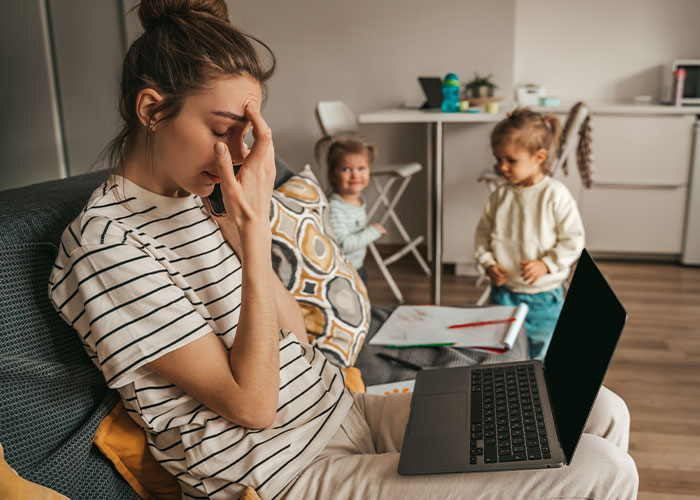Stressed woman managing laptop and two children at home, highlighting take care siblings refuses support mother situation. Stressed woman managing laptop and two children at home, highlighting take care siblings refuses support mother situation.