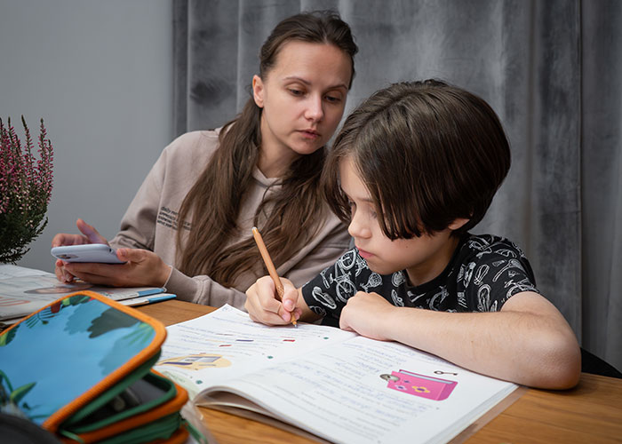 Young woman helping her sibling with homework, showing care and support while refusing assistance from their mother. Young woman helping her sibling with homework, showing care and support while refusing assistance from their mother.