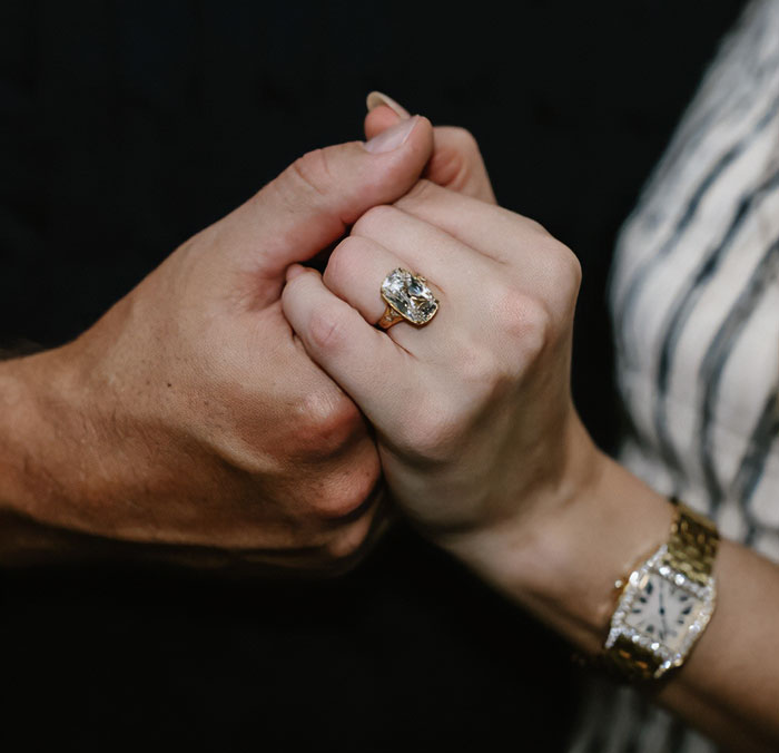 Close-up of two hands holding each other, one wearing a large engagement ring, symbolizing wedding and family moments. Close-up of two hands holding each other, one wearing a large engagement ring, symbolizing wedding and family moments.