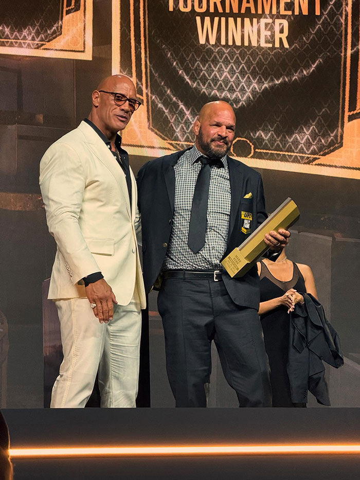 Dwayne Johnson in a white suit at an event with a man holding a UFC award, fans discuss actor’s new slim look and health. Dwayne Johnson in a white suit at an event with a man holding a UFC award, fans discuss actor’s new slim look and health.