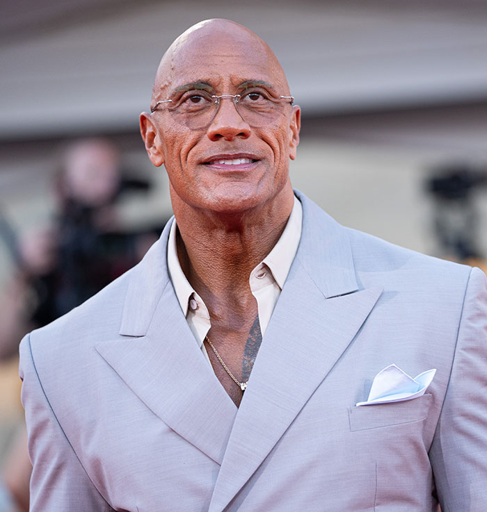 Dwayne Johnson wearing glasses and a light gray suit, attending an event amid fans defending his new slim look. Dwayne Johnson wearing glasses and a light gray suit, attending an event amid fans defending his new slim look.