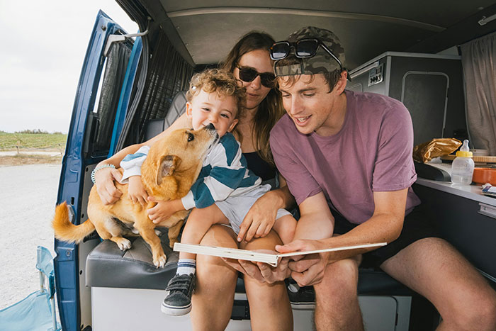 Family with child and dog inside van, enjoying a book together, showing moments that look awesome in movies but are worse in real life.