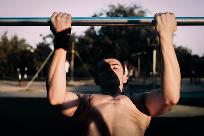Man doing pull-ups outdoors in sunlight demonstrating strength in a scene from relentlessly pursued by someone context