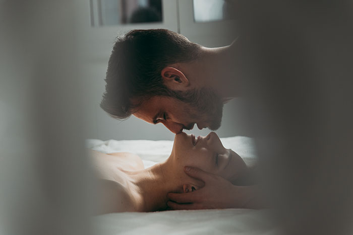 Couple sharing an intimate moment on a bed, illustrating things that look awesome in movies but are often terrible in real life.