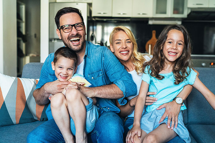 Happy family smiling together on couch at home, illustrating relatable moments in relentlessly pursued by someone scenarios.