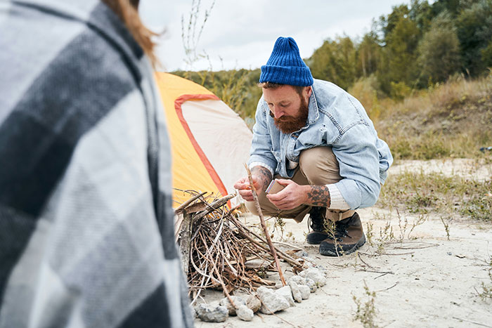 Man wearing blue beanie and denim jacket building a campfire, illustrating scenes from relentlessly pursued by someone in movies.