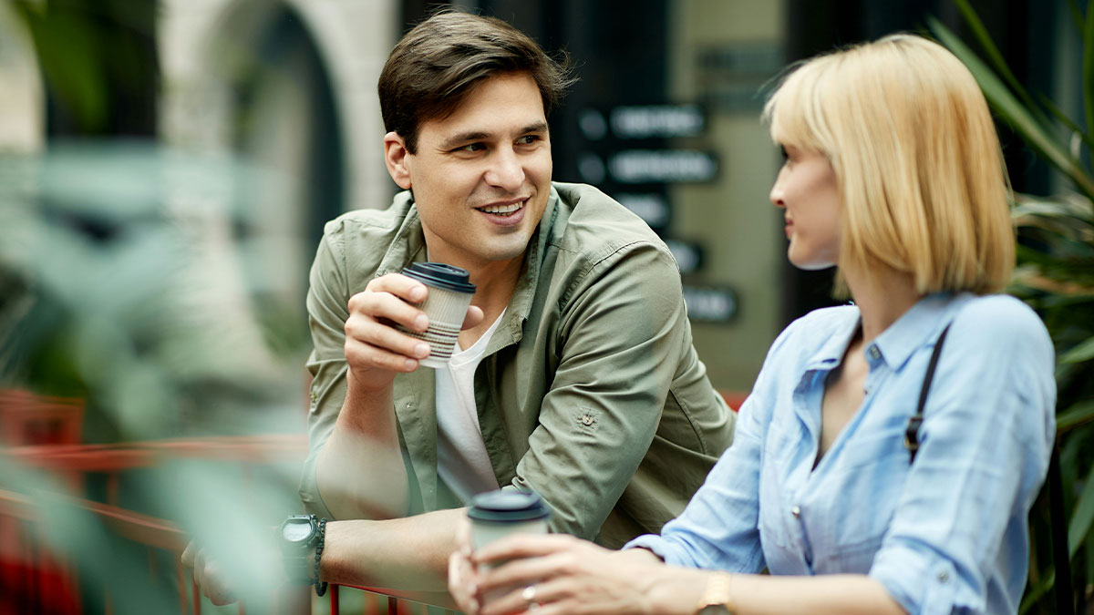 Young man and woman having coffee while chatting outdoors, illustrating things that look awesome in movies but are terrible in real life.