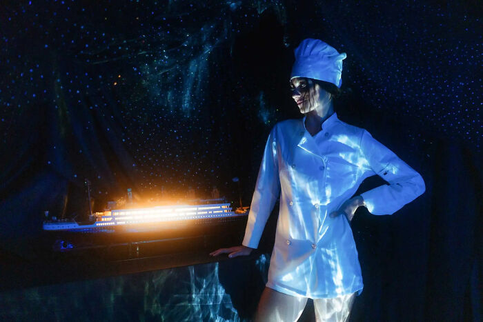 Model in NYC apartment dressed as chef, standing by illuminated Titanic movie set replica with starry night backdrop Model in NYC apartment dressed as chef, standing by illuminated Titanic movie set replica with starry night backdrop