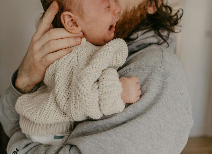 A person gently holding a baby wrapped in a knitted cream sweater, showing a warm and tender moment.