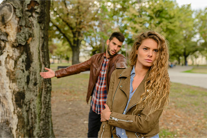 Young tall man pleading with an old friend in a park while she looks upset and crosses her arms. Young tall man pleading with an old friend in a park while she looks upset and crosses her arms.