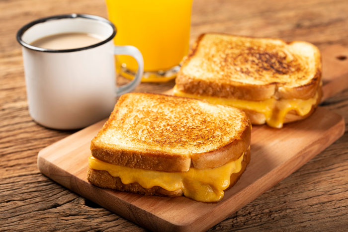 Grilled cheese sandwiches with melted cheddar served on a wooden board alongside coffee and orange juice, employee quits concept. Grilled cheese sandwiches with melted cheddar served on a wooden board alongside coffee and orange juice, employee quits concept.