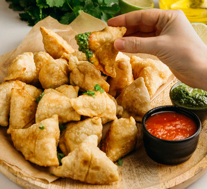 Hand picking crispy fried samosa with green chutney, symbolizing an ambush or surprising act in a workplace scenario. Hand picking crispy fried samosa with green chutney, symbolizing an ambush or surprising act in a workplace scenario.