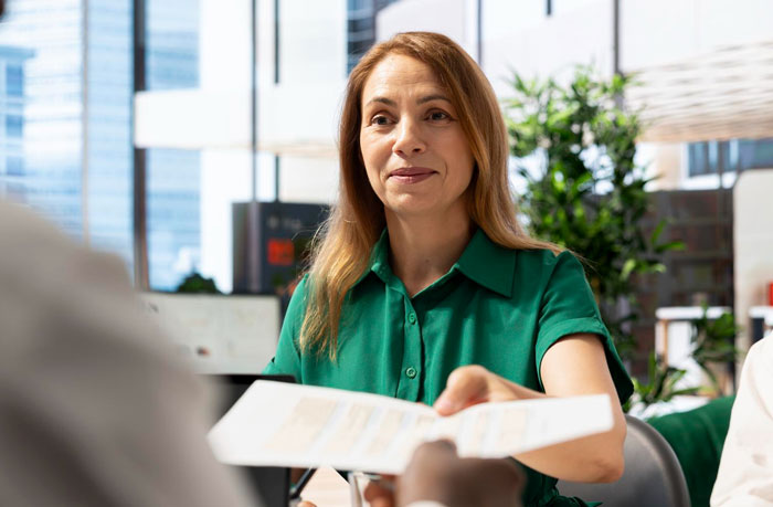 Employee in green shirt handing document during a tense meeting, highlighting workplace ambush and toxic bosses scenario. Employee in green shirt handing document during a tense meeting, highlighting workplace ambush and toxic bosses scenario.