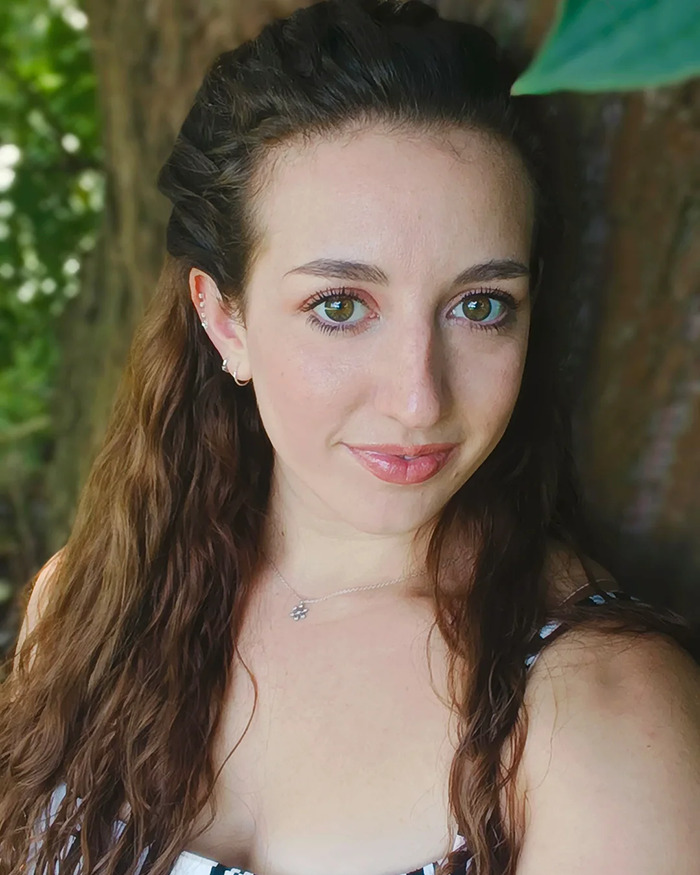 Young woman outdoors with long brown hair, wearing a necklace and striped top, reflecting on trapeze artist incident. Young woman outdoors with long brown hair, wearing a necklace and striped top, reflecting on trapeze artist incident.
