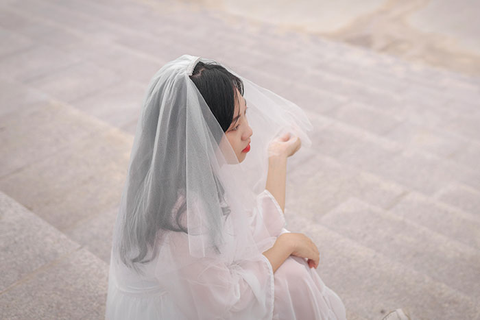 Bride in wedding dress and veil sitting on stone steps, reflecting on choosing who walks her down the aisle.