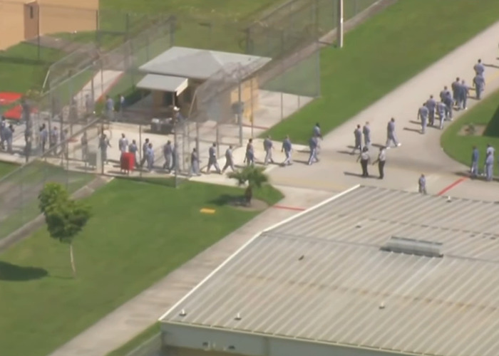 Aerial view of detainees in uniforms walking within a secured facility linked to missing ICE detainee records. Aerial view of detainees in uniforms walking within a secured facility linked to missing ICE detainee records.