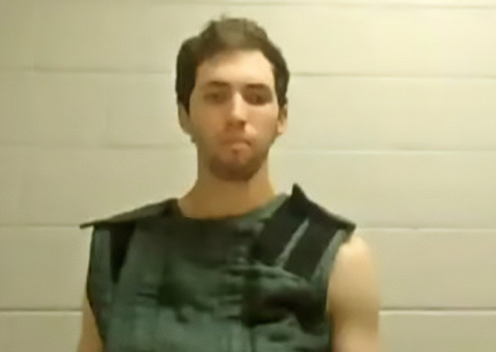 Tyler Robinson appears in court wearing a dark vest, with a neutral expression against a plain background. Tyler Robinson appears in court wearing a dark vest, with a neutral expression against a plain background.