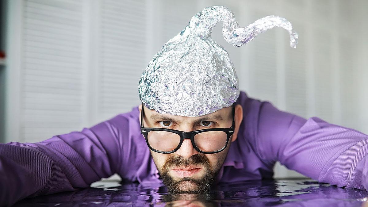Man wearing tinfoil hat and glasses, leaning forward with intense expression, illustrating groups of stupid people concept.