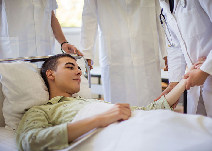 Young male patient in hospital bed being examined by doctors, illustrating unexpected industry secrets in healthcare.