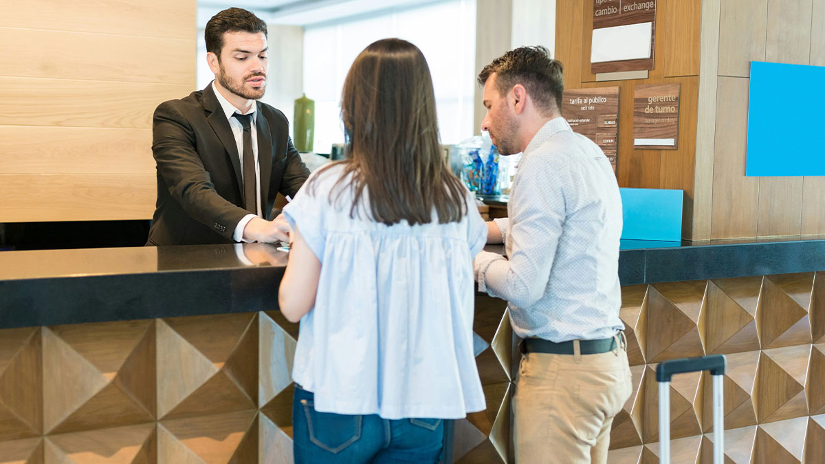 Hotel receptionist assisting a couple checking in, illustrating unexpected industry secrets outsiders donu2019t know about.