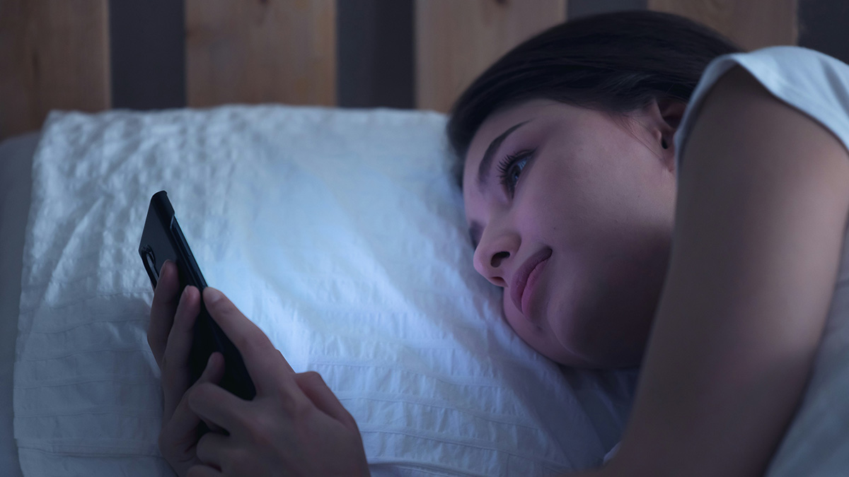 Young woman lying in bed at night, staring thoughtfully at her phone, experiencing paranormal moments.