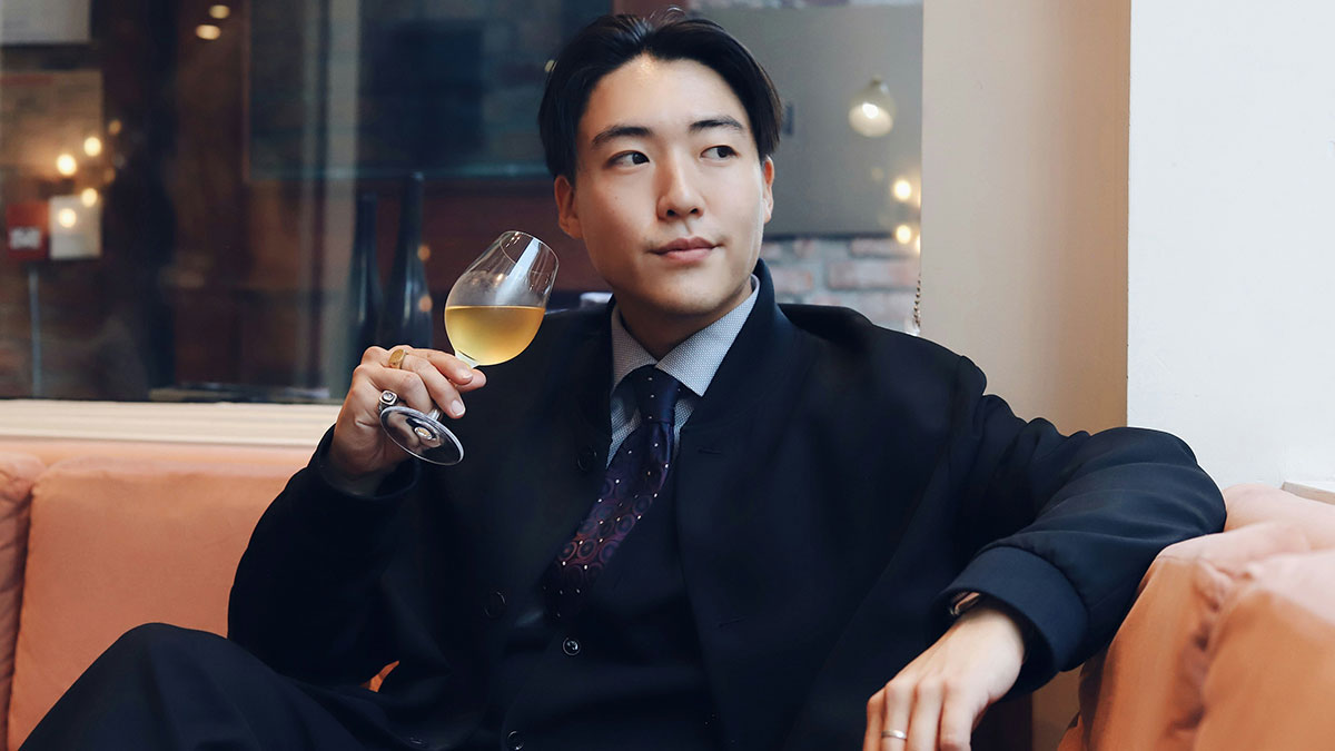 Young man in a suit holding a glass of wine, looking thoughtful while relaxing indoors, reflecting on travel complaints.