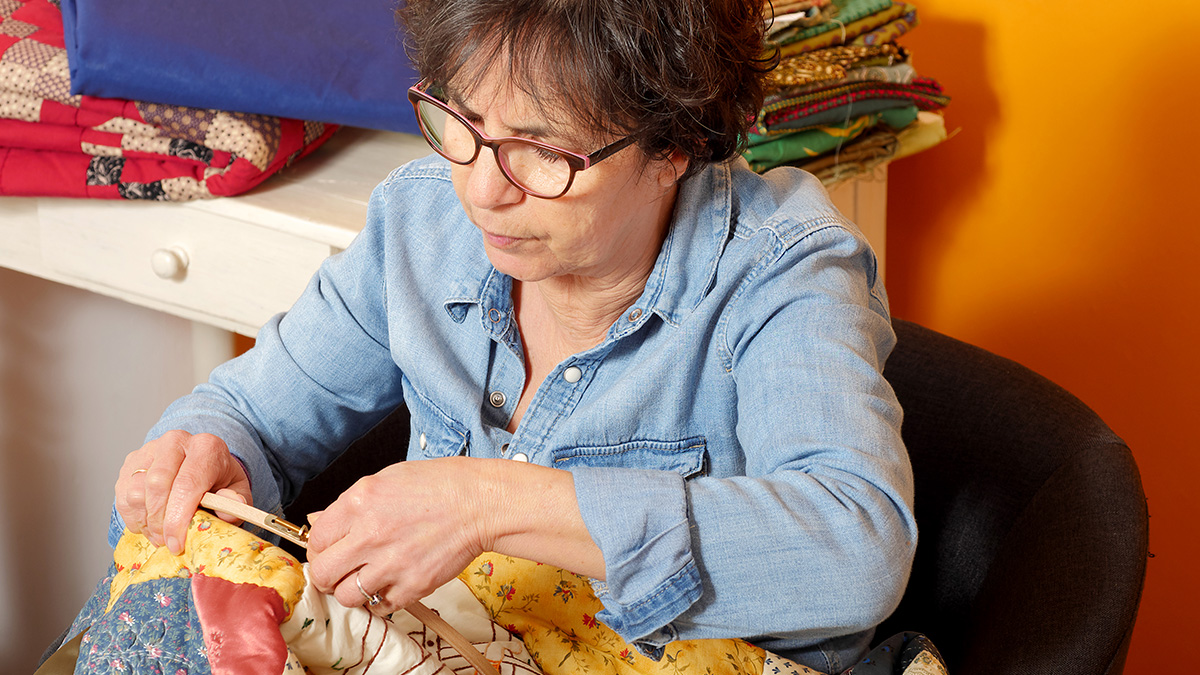 Woman in glasses hand sewing a colorful quilt, depicting a childfree woman upset about a family quilt refusal.