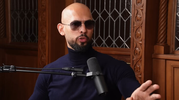 Man in sunglasses and black turtleneck speaking into microphone, sharing insights about falling out of love online.