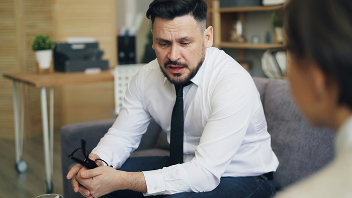 Man in white shirt and black tie holding glasses looking concerned during a serious discussion about teacher scares student incident. Man in white shirt and black tie holding glasses looking concerned during a serious discussion about teacher scares student incident.