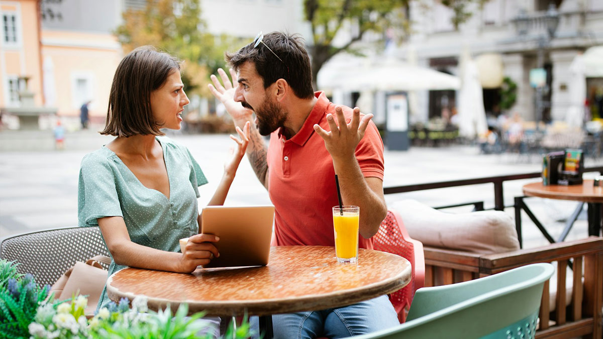 Couple arguing intensely at outdoor cafu00e9 table with tablet and orange juice, illustrating crazy stories servers overheard.