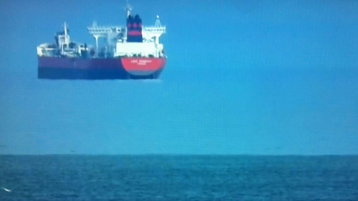 Large ship appearing to float above the ocean surface due to an optical deep sea phenomenon in calm waters.