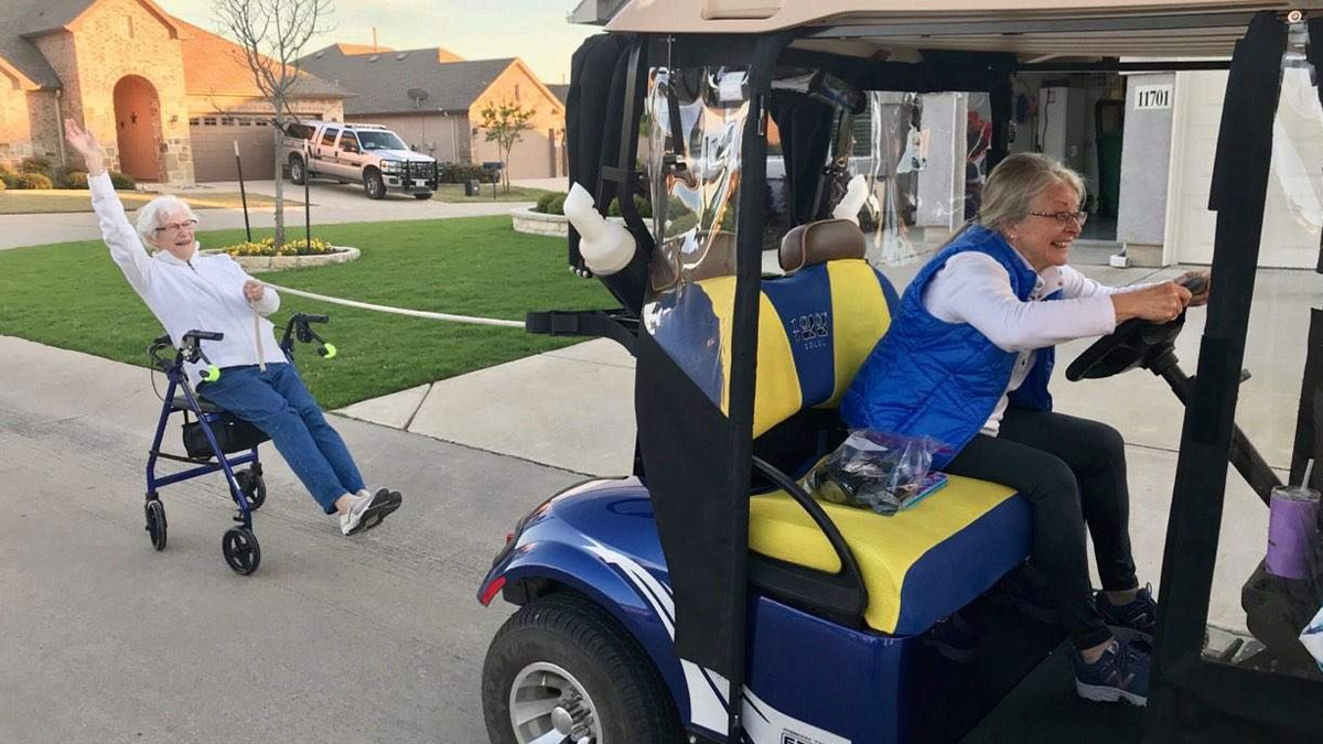 Two funny and wholesome parents playing outside, one driving a golf cart and the other laughing while being pulled along.