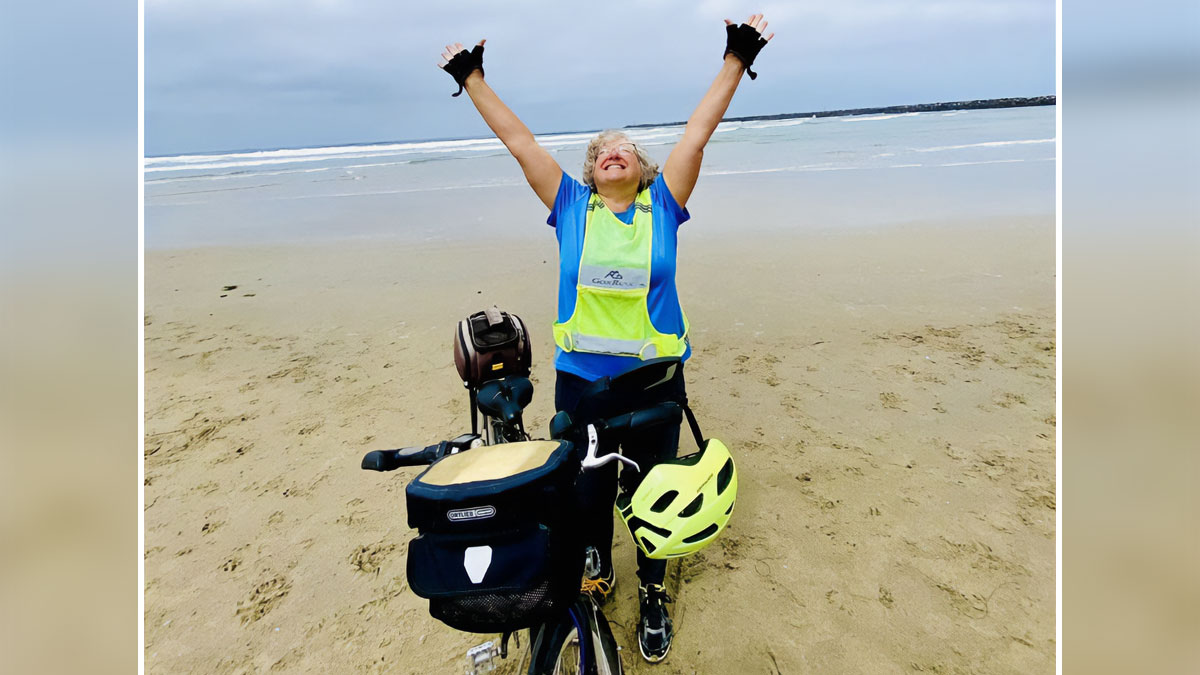 A joyful cyclist raising arms on the beach, enjoying a wholesome moment with bike and helmet on the sand by the ocean.
