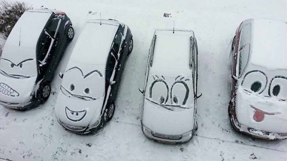 Four cars covered in snow with cartoon faces vandalized on their windshields in playful public property vandalism.