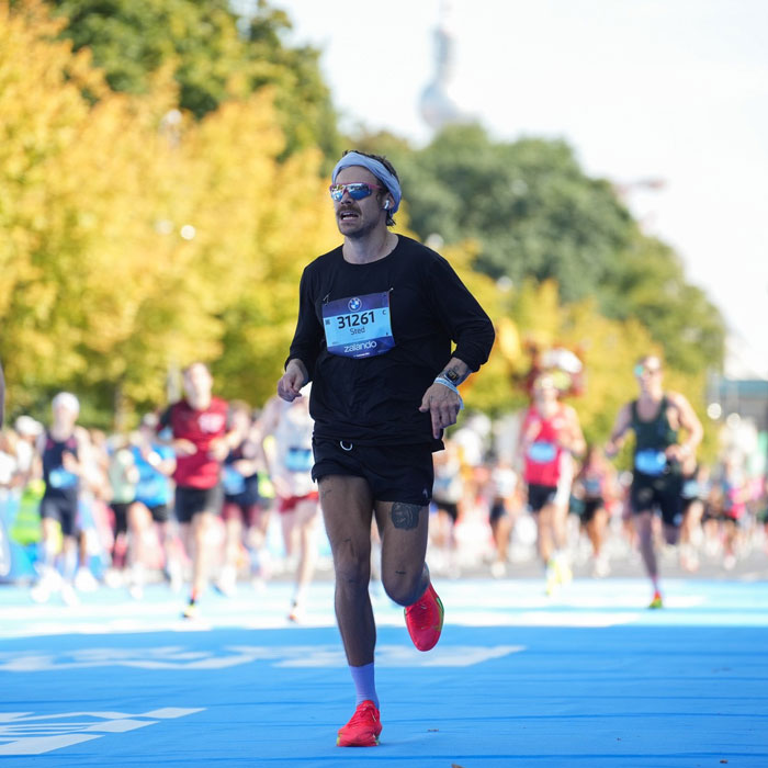 Runner in black outfit and red shoes competing in Berlin Marathon, showcasing impressive speed during the race. Runner in black outfit and red shoes competing in Berlin Marathon, showcasing impressive speed during the race.