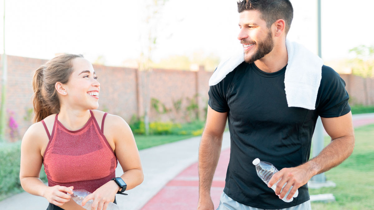 Woman and husband running together outdoors, both smiling and holding water bottles during exercise.