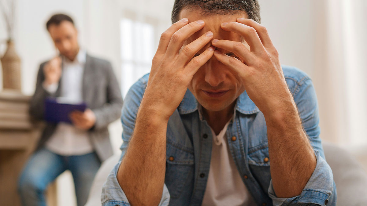 Man in denim jacket stressed during therapy session, dealing with wifeu2019s reaction to attending sisteru2019s baby shower