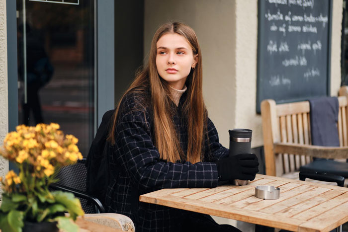 Woman with allergies sitting outside café holding coffee cup, highlighting couple slamming café’s rigid rules. Woman with allergies sitting outside café holding coffee cup, highlighting couple slamming café’s rigid rules.