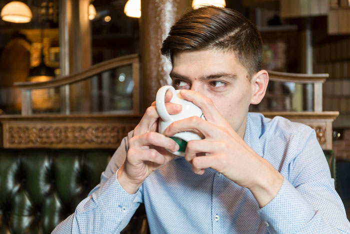 Man drinking coffee inside a café, highlighting issues with café rigid rules after wife with allergies stood outside during date. Man drinking coffee inside a café, highlighting issues with café rigid rules after wife with allergies stood outside during date.