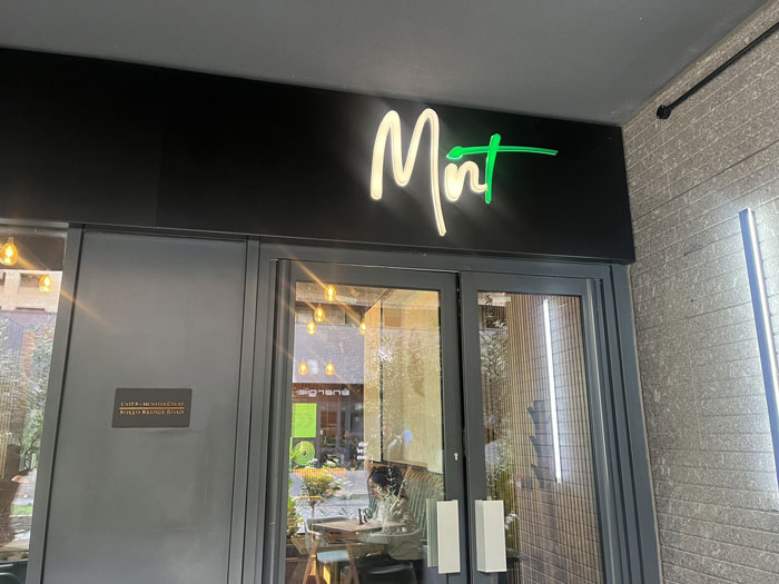 Entrance of Mint café with glass doors and a neon sign, highlighting café rules amid allergic customer controversy. Entrance of Mint café with glass doors and a neon sign, highlighting café rules amid allergic customer controversy.