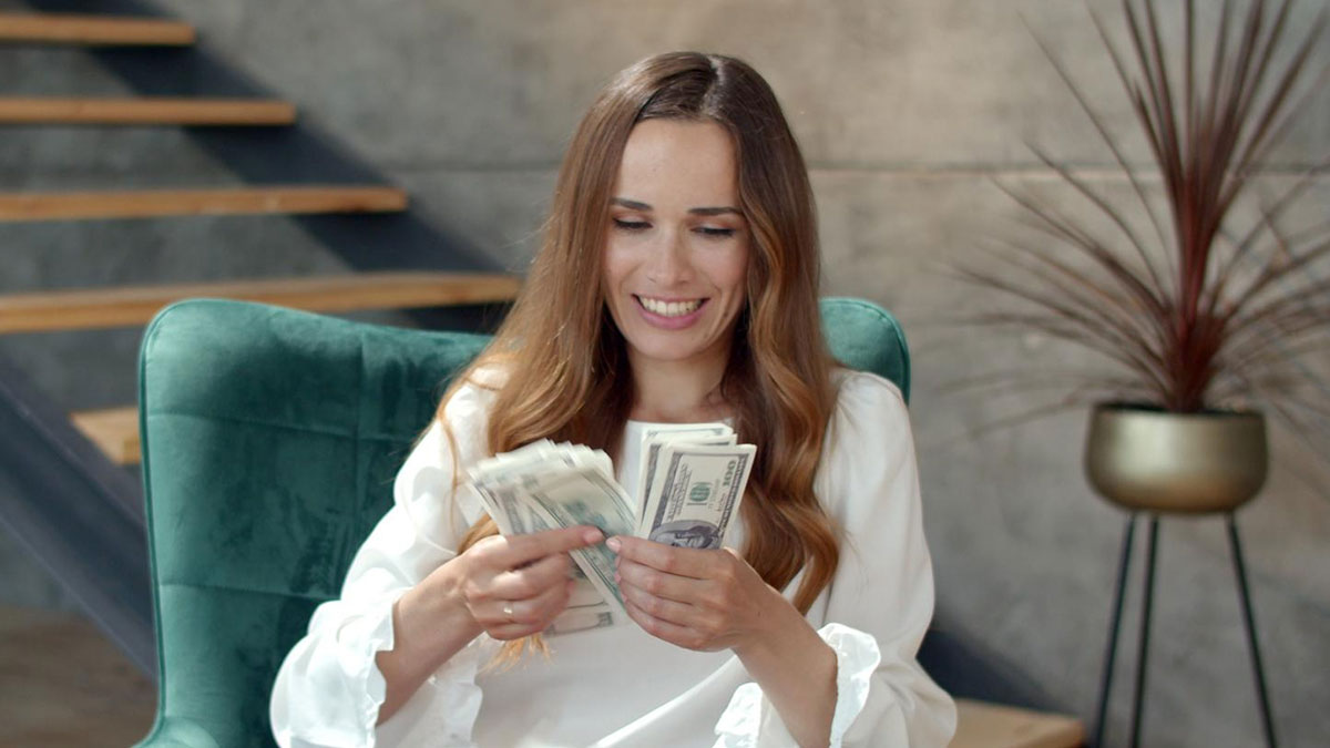 Woman counting money with a smile sitting in a green chair, showing wife turned mean once got money concept.