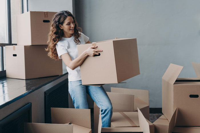 Woman lifting a cardboard box while surrounded by moving boxes, illustrating a wife turned mean once got money scenario. Woman lifting a cardboard box while surrounded by moving boxes, illustrating a wife turned mean once got money scenario.