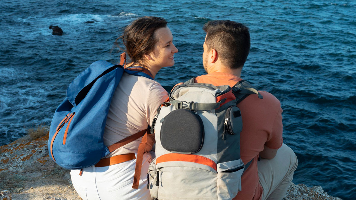 Man with backpack sitting by the ocean shore with a woman, illustrating toxic man romantically involved with two women