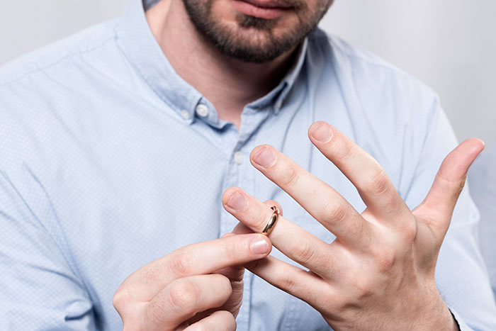 Man in light blue shirt removing wedding ring, symbolizing a woman's world crumbling after husband's dark secret revealed.