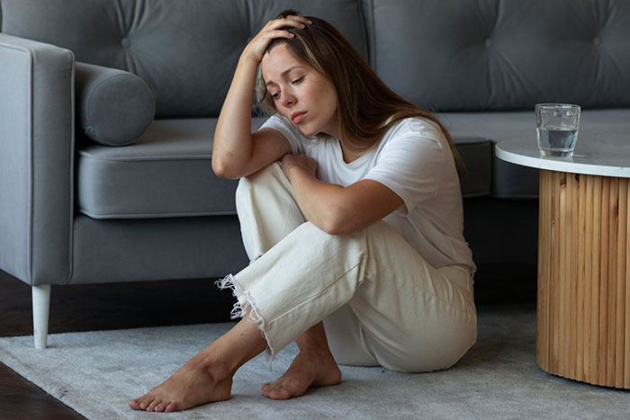 A distressed woman sitting on the floor, holding her head, depicting a woman’s world crumbling after dark marriage secrets.
