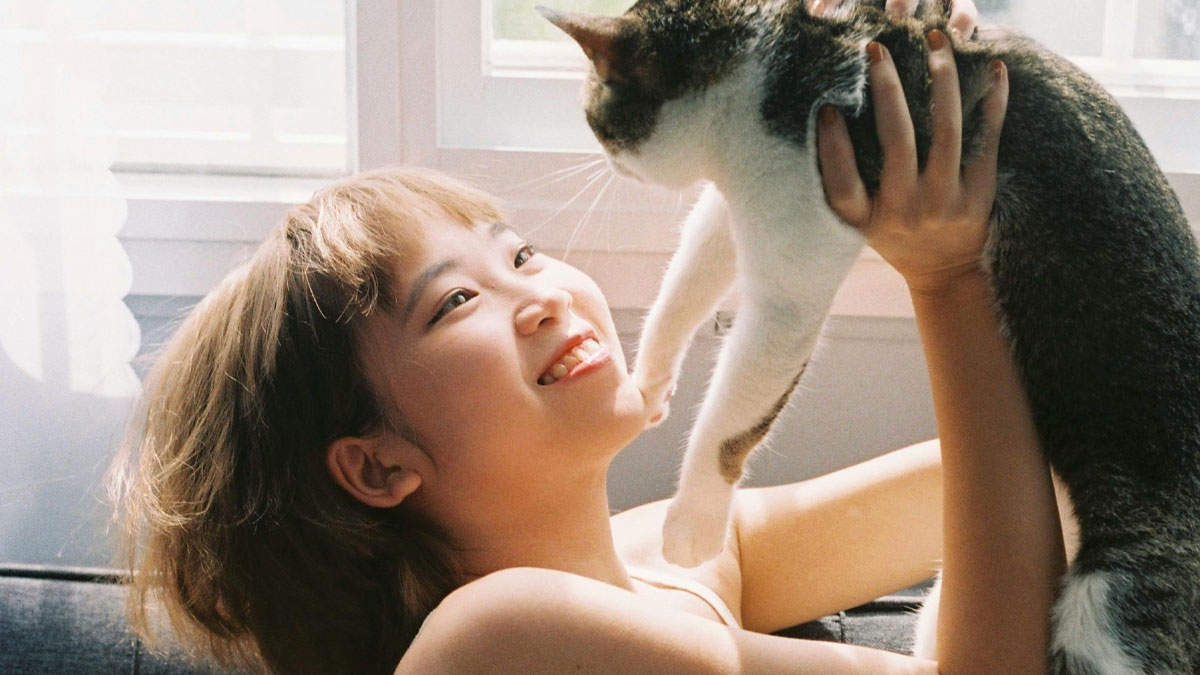 Young woman smiling while holding her cat indoors, highlighting the emotional bond with her pet cat.